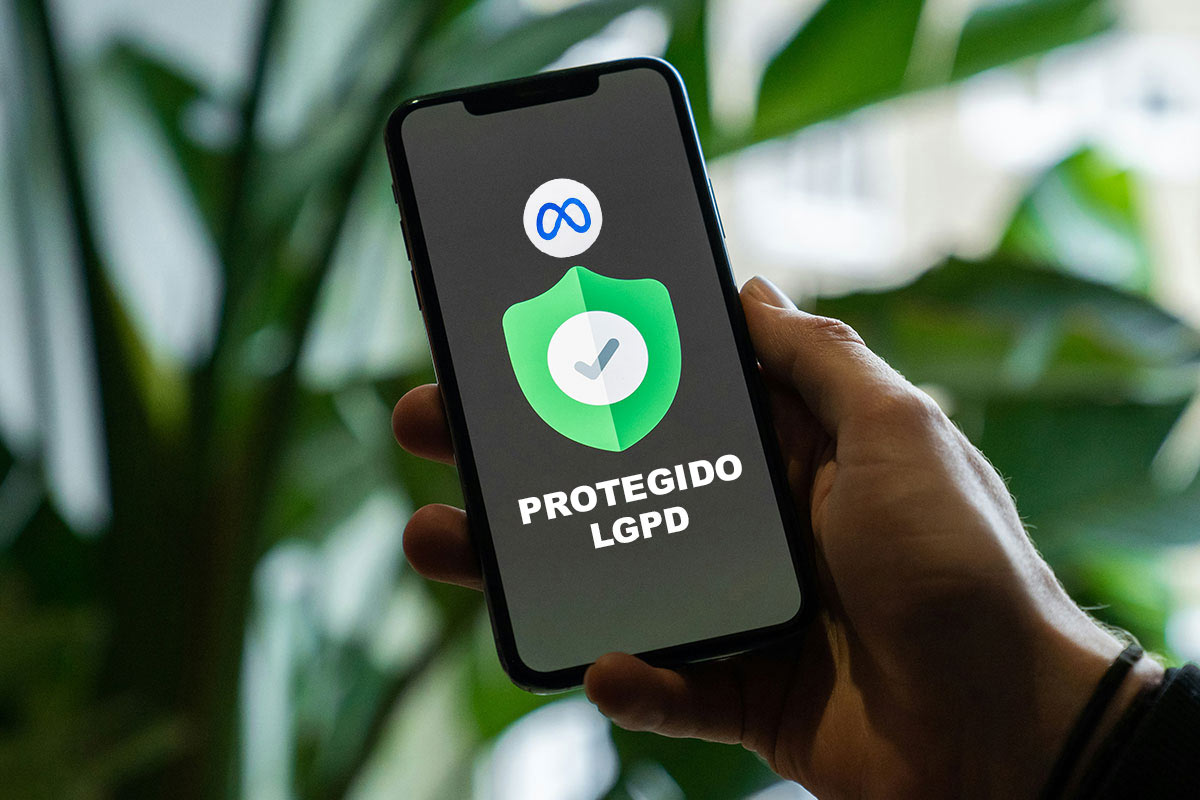 Mão segurando um smartphone com tela preta exibindo o logotipo azul da Meta, um ícone de escudo verde com um símbolo de verificação e o texto 'PROTEGIDO LGPD' em letras brancas, com fundo desfocado de folhas verdes.