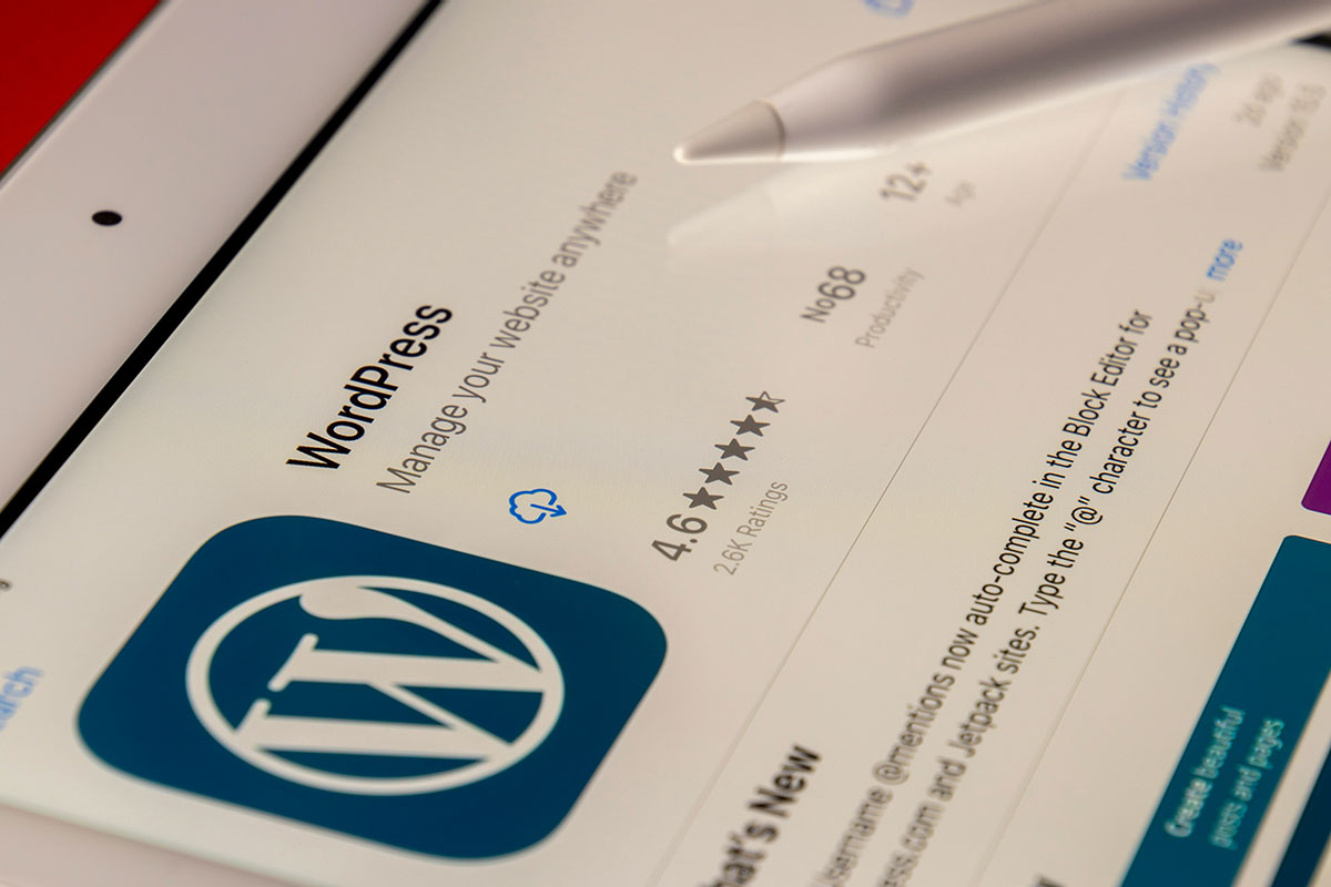 Tela de um tablet exibindo a página de download do aplicativo do WordPress na App Store com uma caneta digital branca apoiada sobre a superfície, destacando o logotipo azul da plataforma.