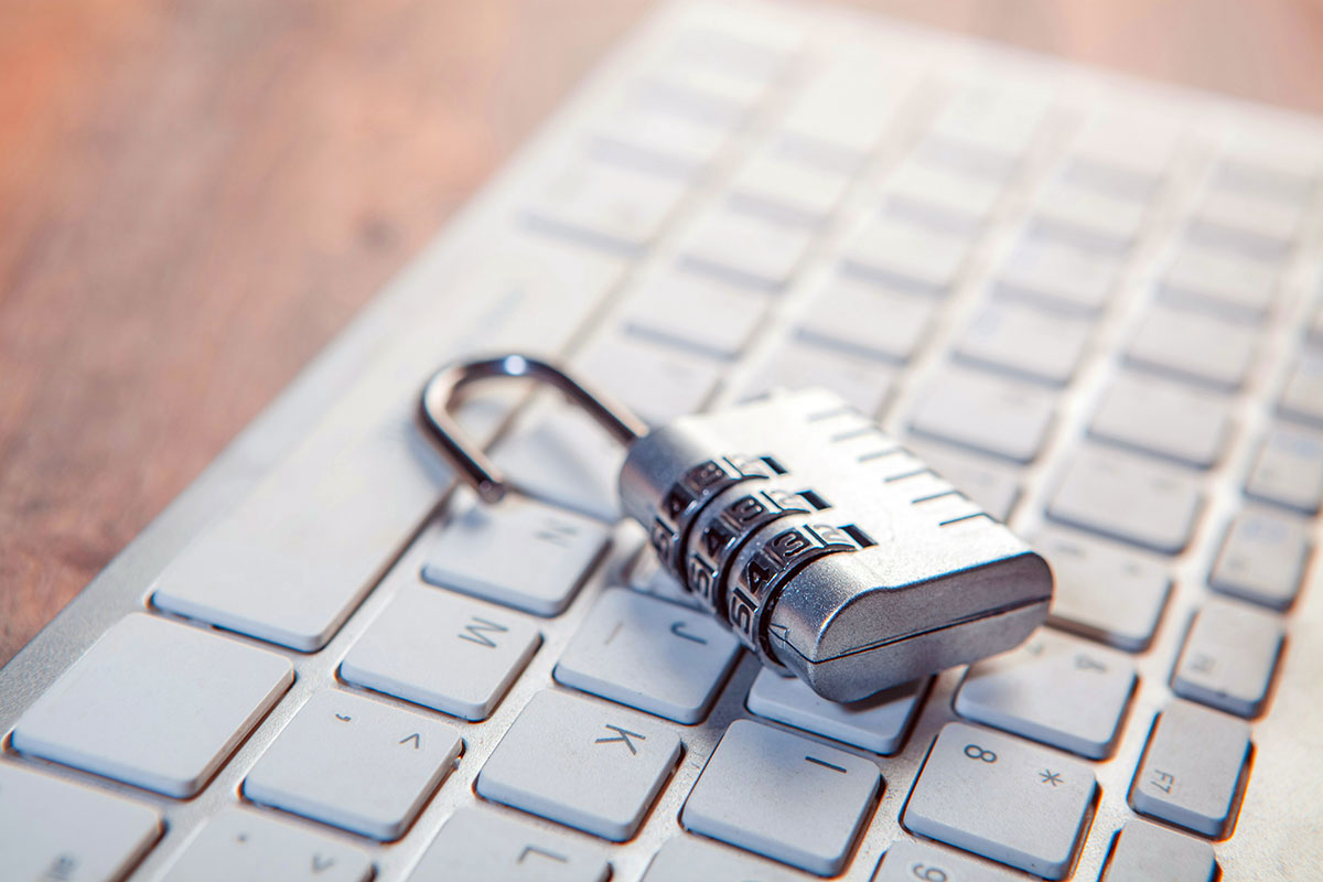 Um cadeado de combinação de metal aberto repousando sobre as teclas de um teclado de computador branco em uma mesa de madeira, simbolizando segurança digital.