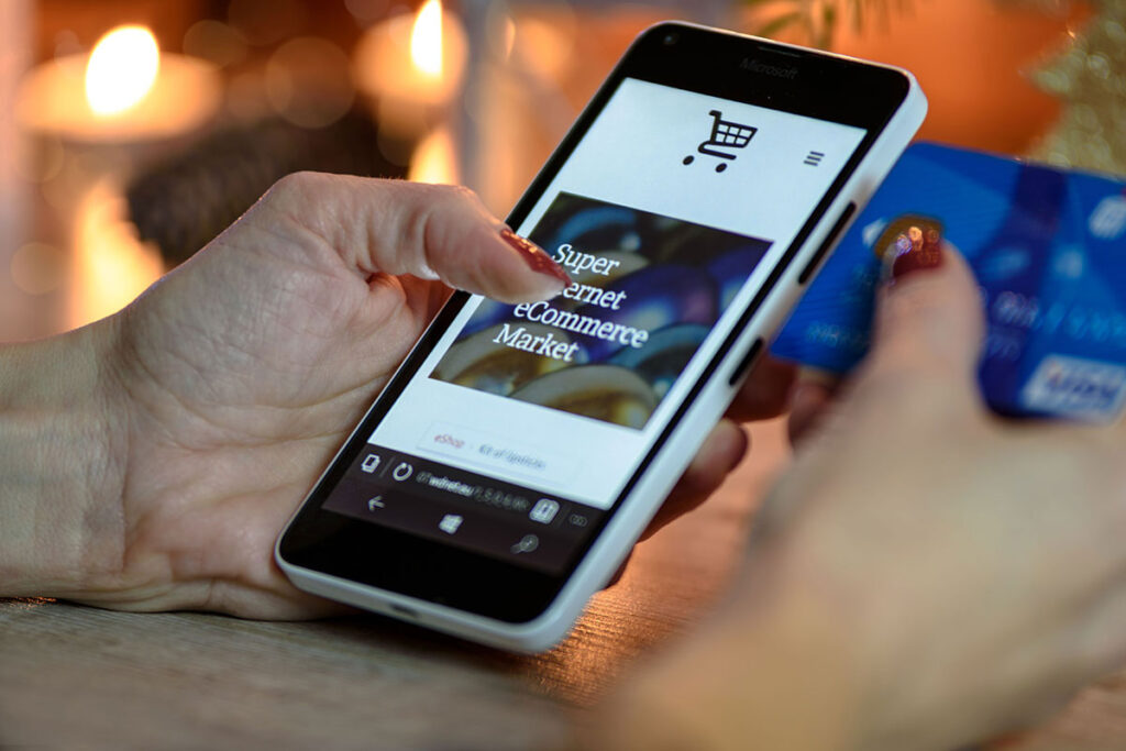 Mãos de uma pessoa segurando um smartphone que exibe uma loja virtual, enquanto segura um cartão de crédito com a outra mão, simbolizando uma compra online rápida e segura.