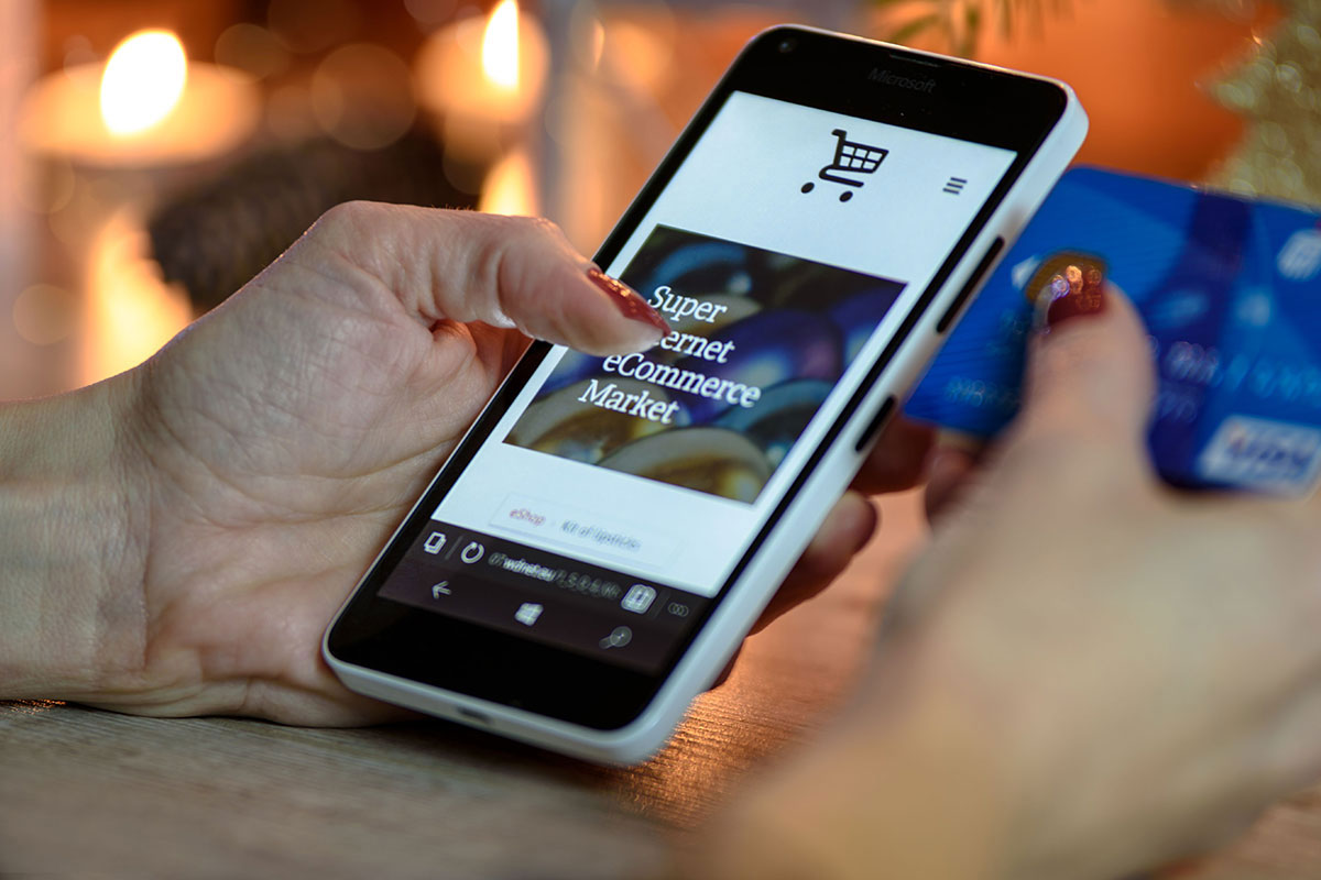 Mãos de uma pessoa segurando um smartphone que exibe uma loja virtual, enquanto segura um cartão de crédito com a outra mão, simbolizando uma compra online rápida e segura.
