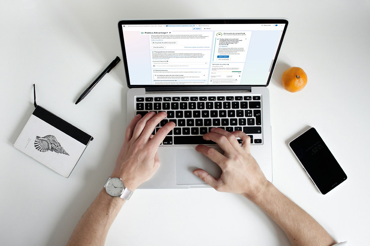 Visão aérea de um profissional trabalhando em um notebook sobre uma mesa branca clean, exibindo a tela do Gerenciador de Anúncios da Meta na seção de configuração do Público Advantage+.