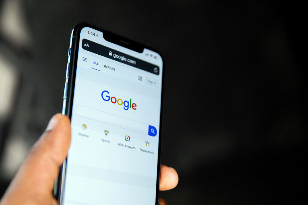 Mão segurando um smartphone que exibe a página de busca do Google na tela, ilustrando o ecossistema de anúncios e transparência de IA no Google Ads.