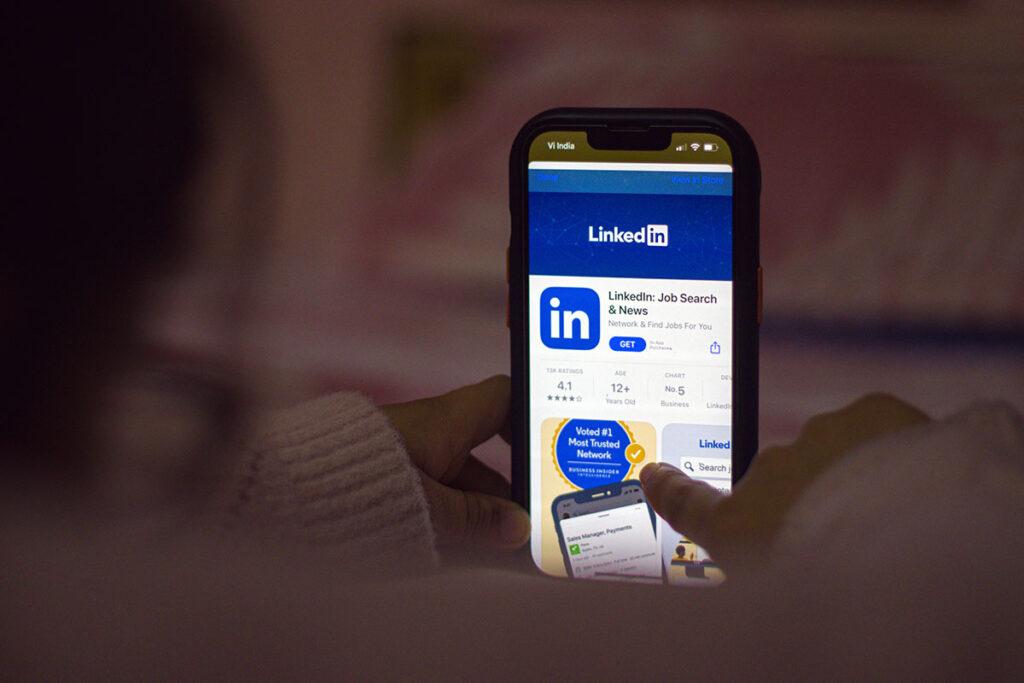 Dedo de um usuário tocando na tela de um smartphone para fazer o download ou atualizar o aplicativo mobile oficial do LinkedIn na loja de aplicativos virtuais.