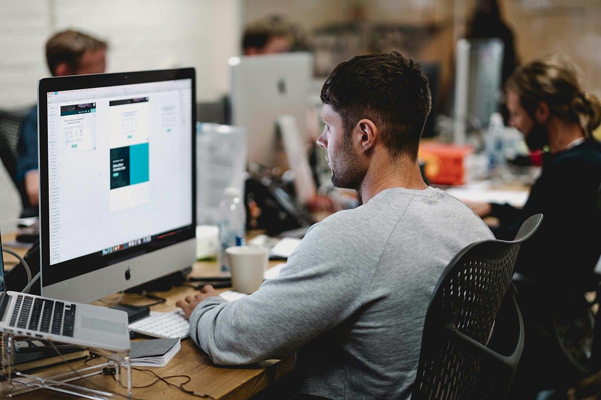 Profissional de web design trabalhando na criação e otimização do layout de um site em seu computador.