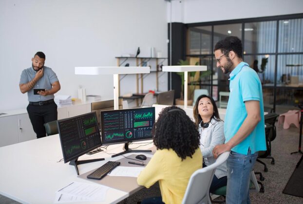 Equipe de marketing e dados em escritório moderno analisando dashboards em monitores duplos.